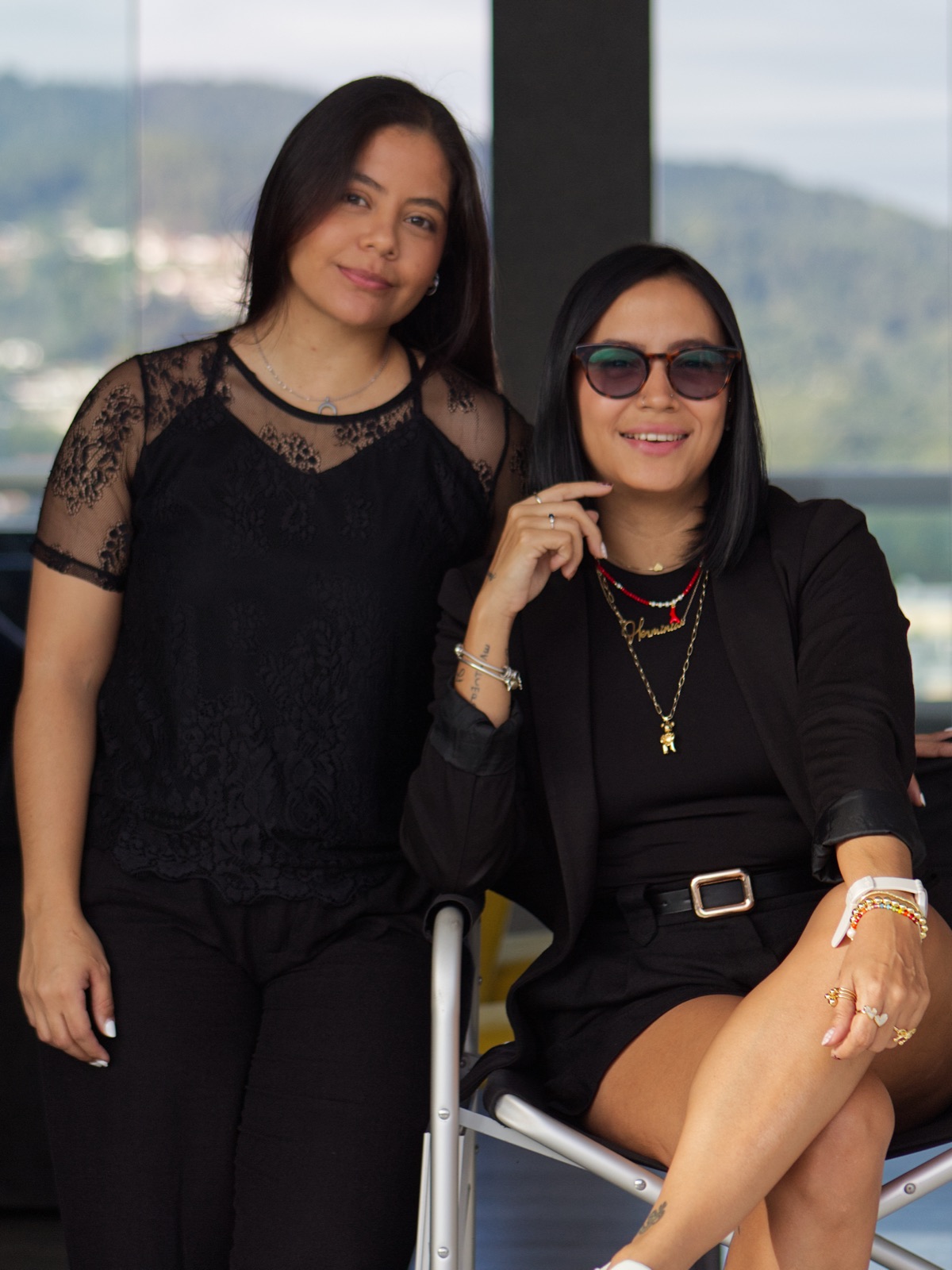Herminia Abreu, sentada a la derecha, junto a su compañera de equipo, de pie con una blusa de encaje negra, en una terraza